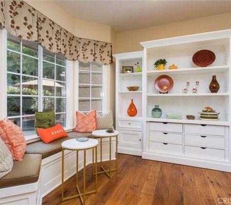 A bright white kitchen featuring a cozy window seat and open shelves for storage and display.