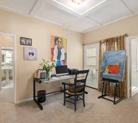 A cozy home office featuring a desk, chair, and colorful paintings on the walls.