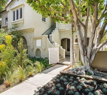 A house surrounded by a tree and bushes in the foreground, showcasing a serene residential setting.